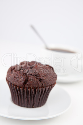 Chocolate muffin and a cup of coffee with a spoon on white plate