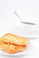 Waffles and a cup of coffee with a spoon on white plates