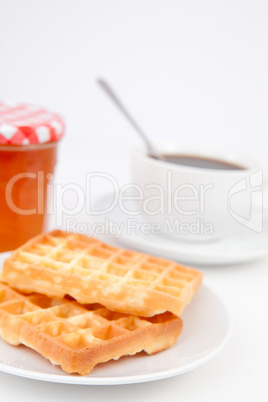 Waffles and cup of coffee with a spoon on plates and a pot of ja