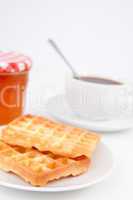 Waffles and cup of coffee with a spoon on plates and a pot of ja