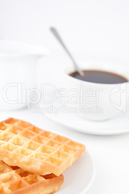 Waffles and a cup of coffee with a spoon on white plates and mil