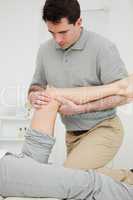 Serious physiotherapist looking at the knee of a patient