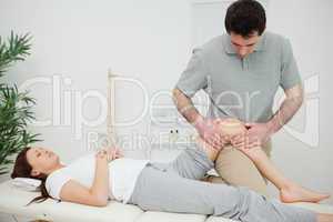 Black-haired osteopath touching the knee of a patient