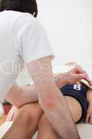 Chiropractor pressing his arm on the thigh of his patient