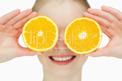 Close up of a cheerful woman placing oranges on her eyes