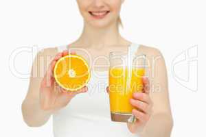 Woman presenting an orange while holding a glass