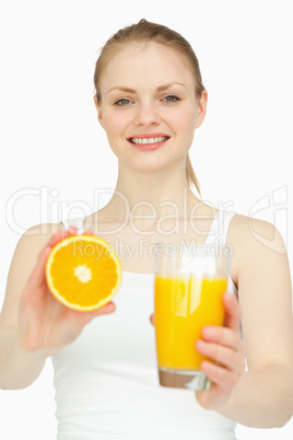 Smiling woman holding a glass while presenting an orange