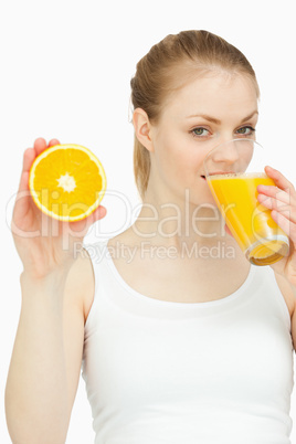 Woman drinking in a glass while presenting an orange