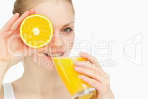 Woman placing an orange on her eye while drinking