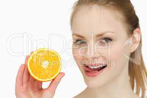 Woman holding an orange while placing her tongue on her lips