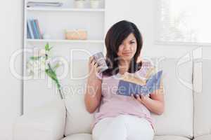 Woman sitting on a sofa while she is holding a mug and a book