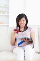 Woman looking ahead as she reads a magazine and holds a glass of