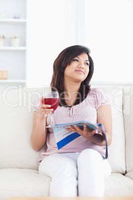 Woman sitting on a couch while holding a glass of red wine and a