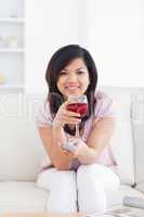 Woman holding a television remote while holding a glass of red w