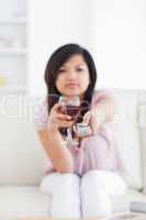 Blurred woman holding a glass of red wine and a television remot