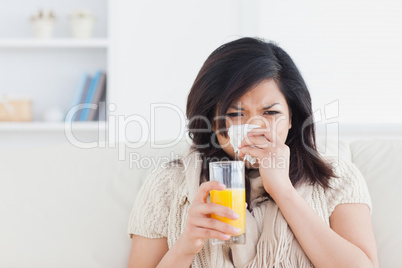 Woman holding a glass of orange juice while sneezing