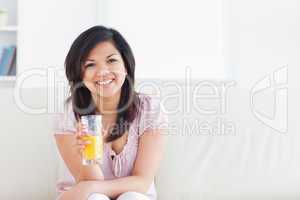 Woman smiling and sitting in a couch while holding a glass of or