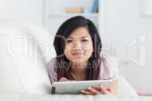 Woman typing on a tablet while resting on a couch