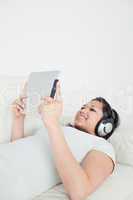 Woman lying on a sofa with headphones on and holding a tactile t