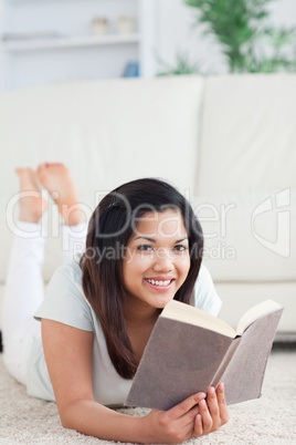 Smiling woman lying on the floor while reader a book
