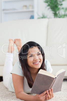 Woman smiling and holding a book as she lays on the floor