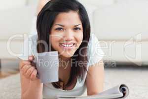 Smiling woman on the floor holding a mug and a magazine