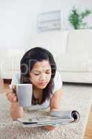 Woman holding a mug while reading a magazine on the floor