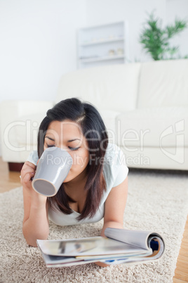 Woman drinking from a mug while holding a magazine