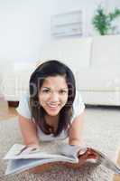 Woman laying on the floor and smiles as she holds a magazine