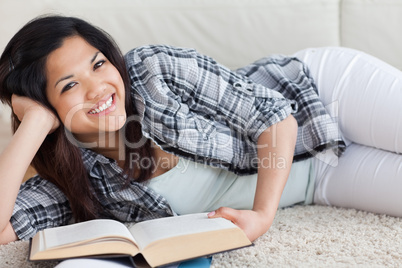 Woman smiling and holding a book as she lies on the floor