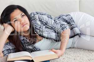 Thinking woman lying on the floor while holding a book