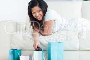 Woman laying on a sofa while holding up clothes from a shopping