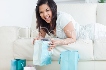 Woman holding up a shopping bag while lying on a sofa