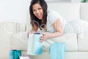 Woman holding up a shopping bag while lying on a sofa