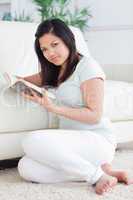 Woman sitting in front of a sofa while reading a book