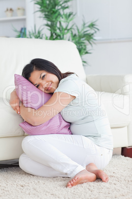 Smiling woman holding a pillow while sitting on the floor