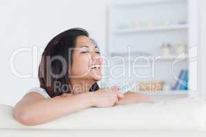 Laughing woman holds a remote and laughs as she stands on a sofa
