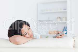 Woman with a remote on her hand resting her head on a white couc