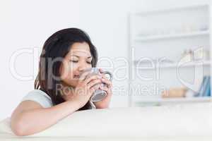 Woman drinking from a mug as she rests one arm on a sofa