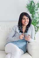 Woman sitting on a couch while holding a grey mug