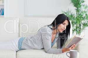 Woman lying on a sofa while reading a book