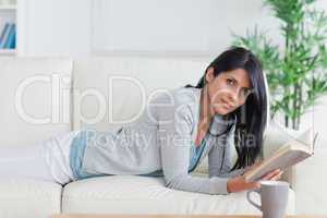 Woman laying on a sofa while reading a book