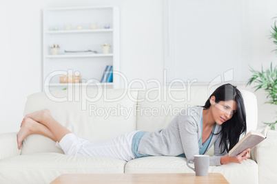 Woman lying on a sofa while reading a book and crossing her legs