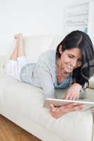 Smiling woman lying on a couch and plays with a tactile tablet