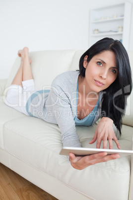 Woman lying on a sofa while playing with a tablet