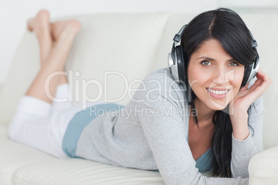 Woman smiling with headphones on while lying on a sofa