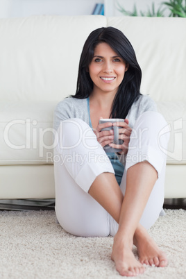 Woman holding a mug with two hands and crossing her legs while s