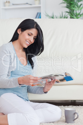 Smiling woman holding a magazine with a mug on the floor