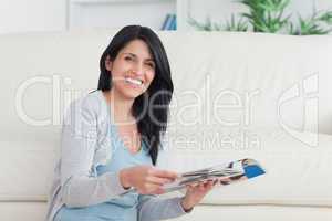 Smiling woman holding a magazine while leaning on a couch