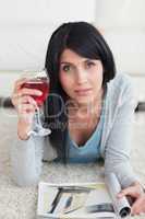 Woman lying on the floor while holding a glass of wine and a mag